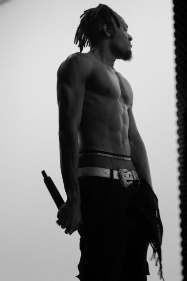 Shirtless person standing sideways, holding an object, in a high-contrast setting.